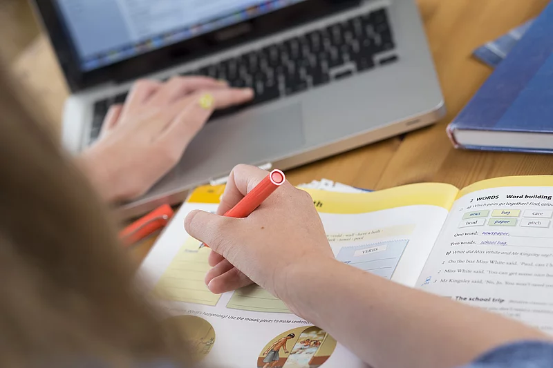 Kind bei den Schulaufgaben am Tisch mit Heft und Laptop
