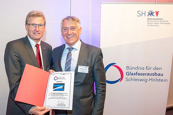 2 Herren bei der Übergabe einer Urkunde während eines Pressetermins mit dem Ministerium für Wirtschaft, Verkehr, Arbeit, Technologie und Tourismus des Landes Schleswig-Holstein 