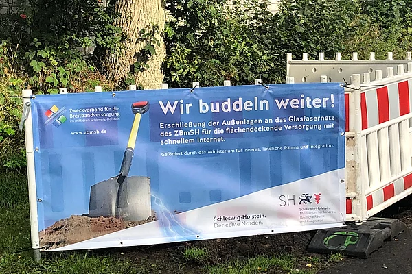 Plakat mit der Aufschrift "wir buddeln weiter" an einer Baustellenabsperrung