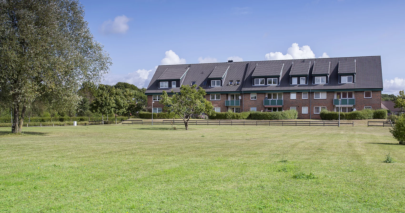 Foto eines Mehrfamilienhaus mit grüner Wiese im Vordergrund