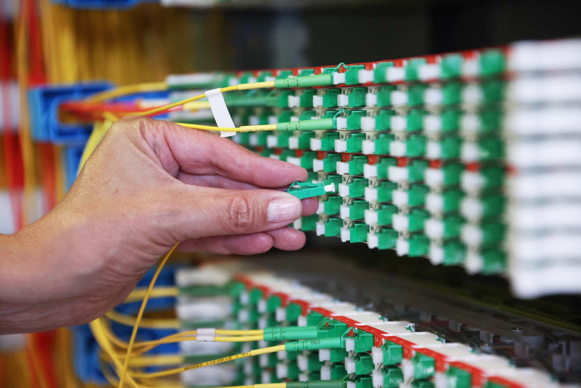 Eine Hand steckt ein Glasfaserkabel in einem Verteilerkasten innerhalb des POP